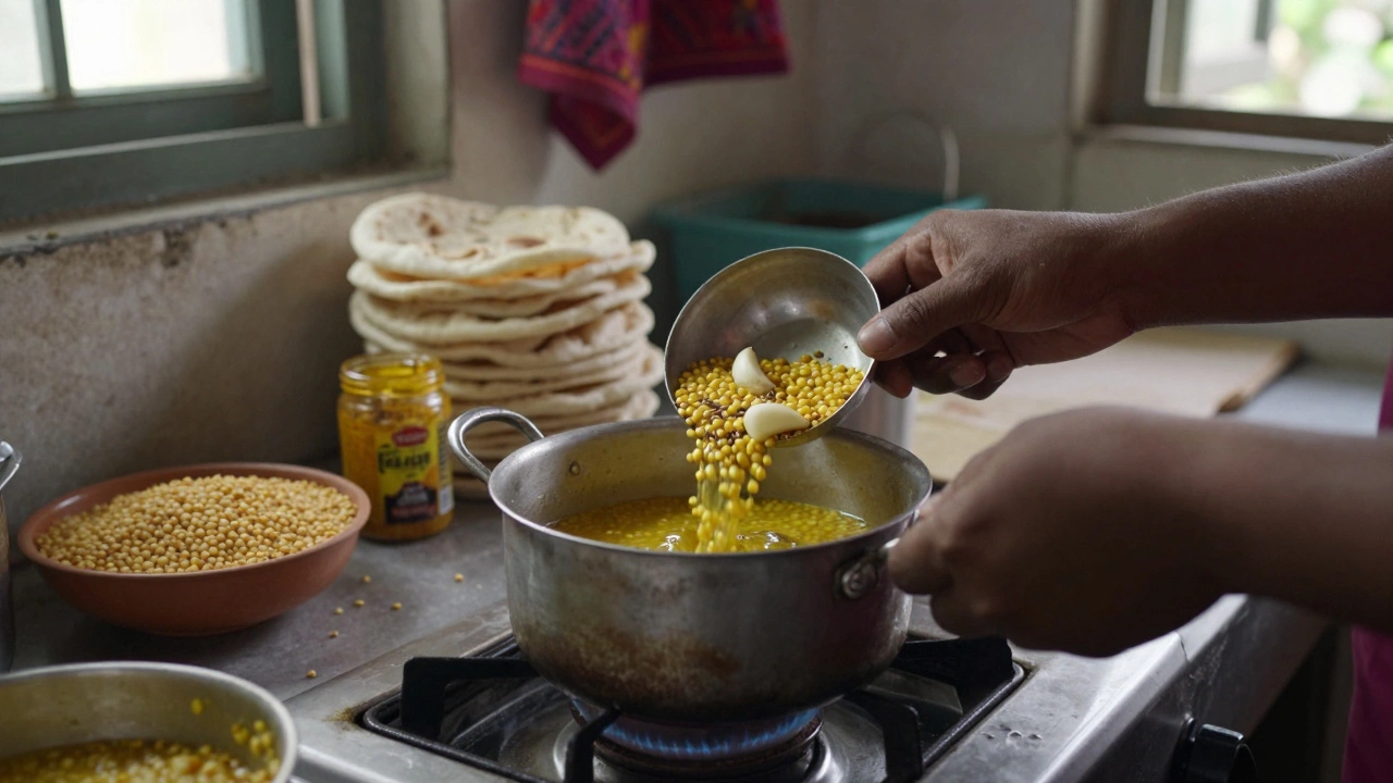 Hands pouring cumin and garlic tadka into simmering lentils in a small pot on a stove.